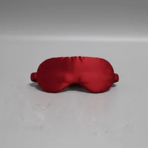 Red satin sleep mask with elastic strap on neutral background.